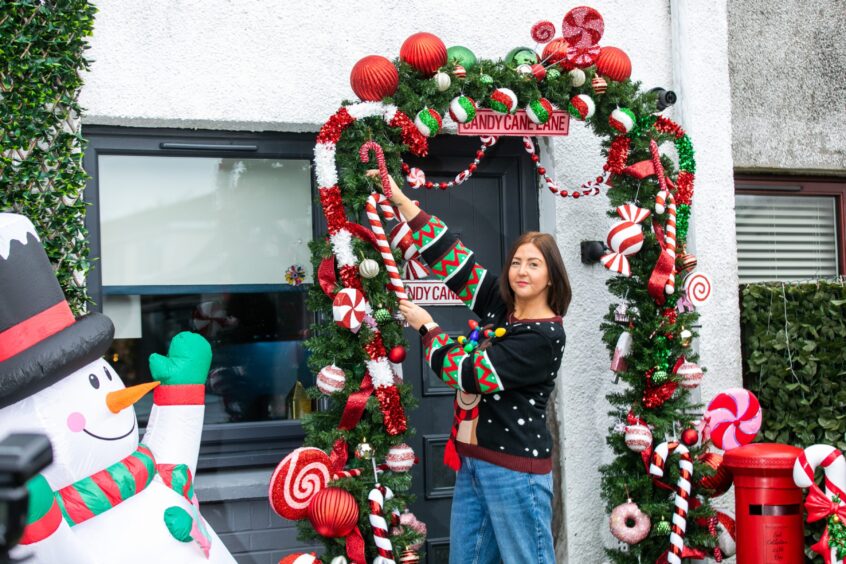 A giant inflatable snowman sits on the left as Caris Rose decorates her front door with artificial peppermints and candy canes.