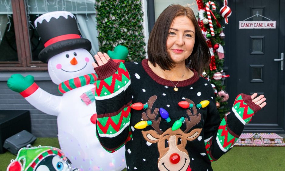 Caris Rose waves at the camera wearing a Christmas-themed jumper. Behind her is an inflatable snowman and her front door decorated with candy canes.