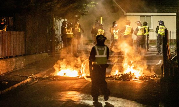 Police officers watch the street fires in Kirkton