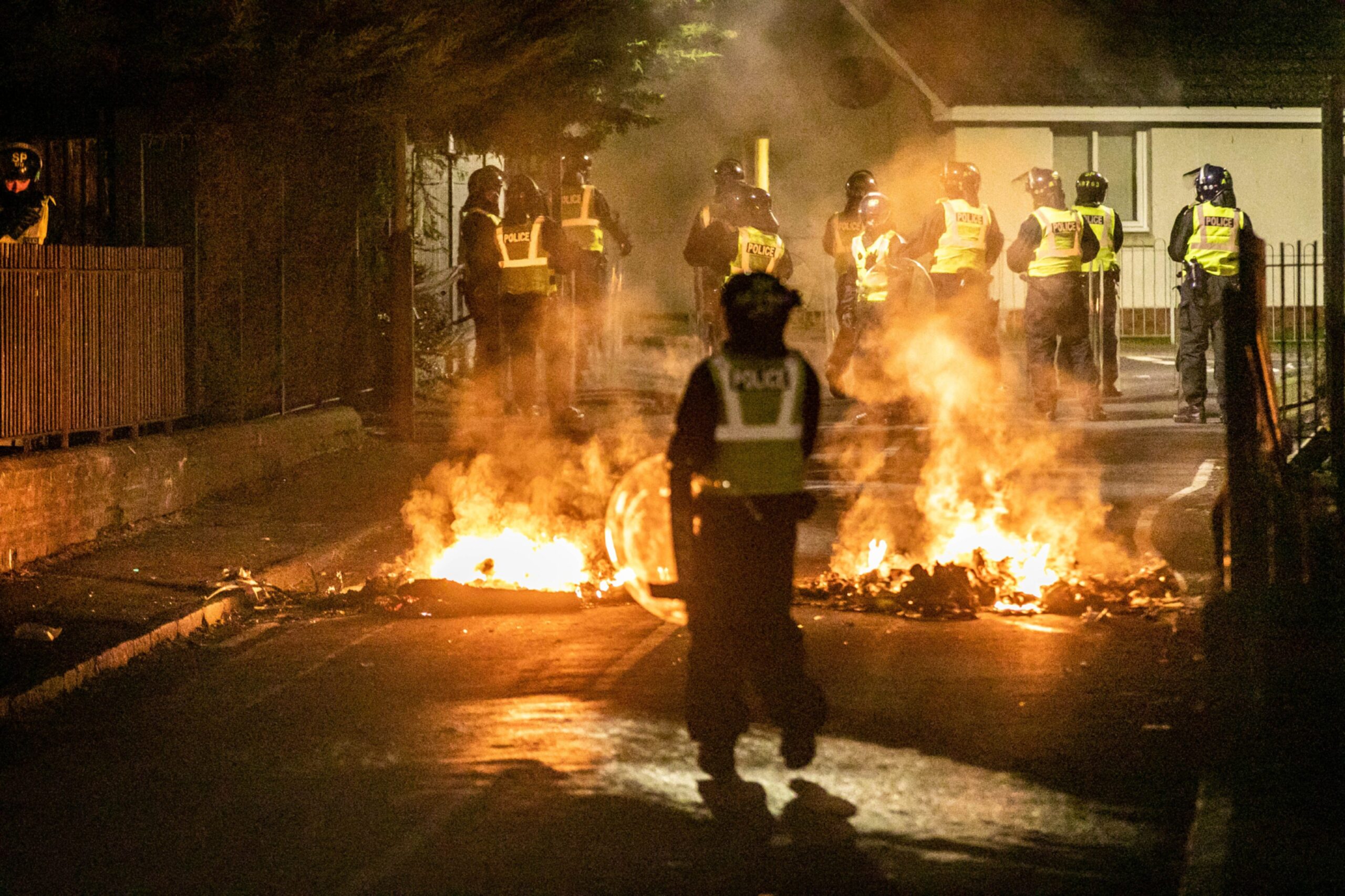 Police officers watch the street fires in Kirkton