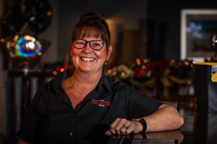 Carol-Anne Key, front of house at the Red House Hotel, smiles at the camera with one armed leaning against the bar.