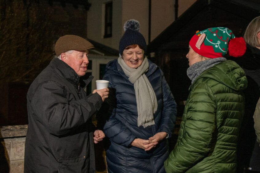 Two women in hats and an older gentleman in a flat cap talking outside one of the windows