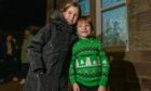 Two young children in warm coat and Christmas jumper outside an illuminated window with a Jack Frost design in the Craigie area of Perth.