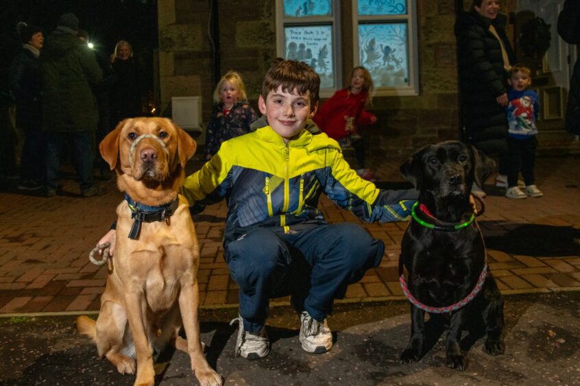 A young boy Robbie Martin, 11, with Labradors Morlich and Jura outside a house with illuminated window and group of onlookers 