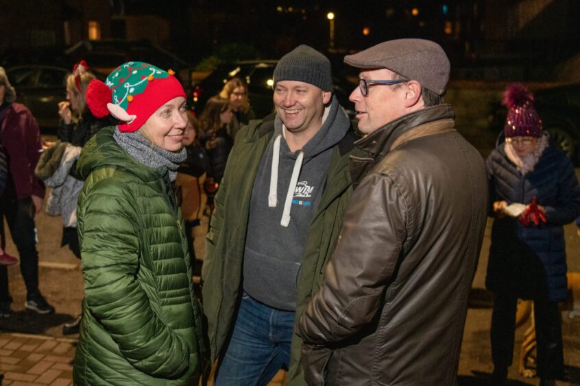 Woman in woollen elf style hat talking to two men as part of a crowd of onlookers in Wilson street, Craigie