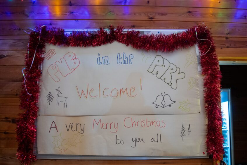 Handwritten, tinsel covered sign, which reads 'Pub in the park, welcome! A very merry Christmas to you all'.