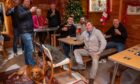 Group of seven men sitting around wooden tables in the Glenfarg tennis pavilion raising pints to the camera.