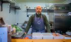 Orkun Cevik standing in his shack surrounded by food and appliances.