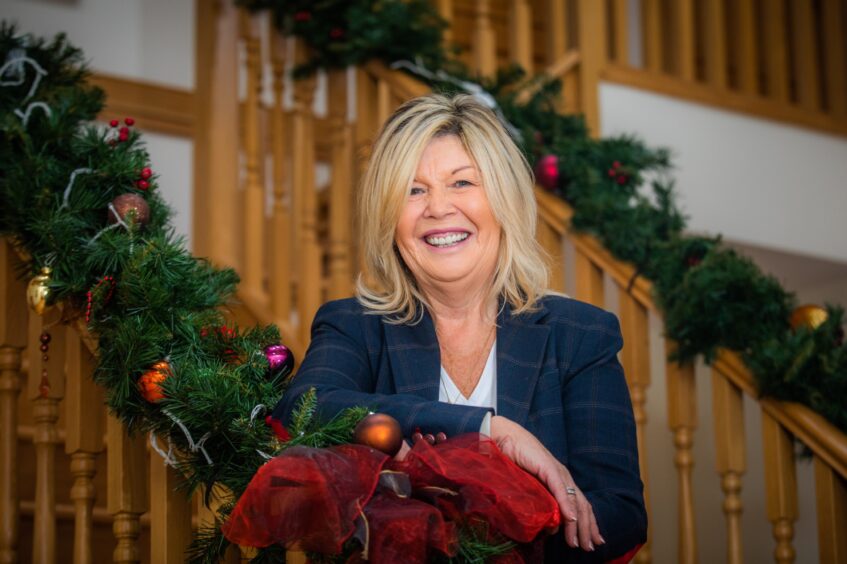 Lynda Mulholland standing next to a staircase, wrapped in Christmas decorations. 