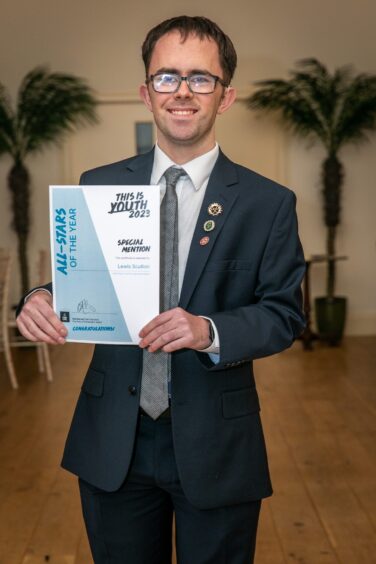 Lewis Scullion in smart dark suit and tie smiling holding his certificate