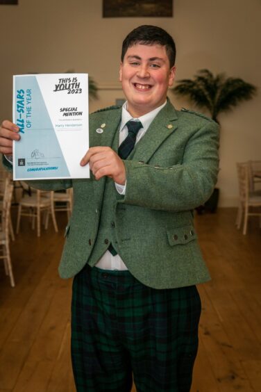 Harry Henderson in smart tweed jacket holding certificate with a huge smile
