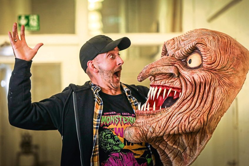 Image shows mask-maker Keith Robson looking terrified by one of his handmade masks. 
