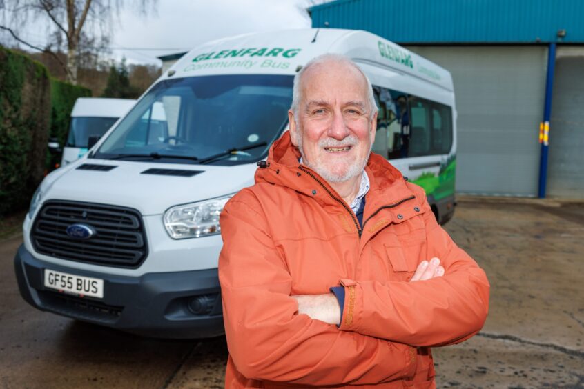 Douglas Fraser, arms folded, standing in front of a minibus with Glenfarg community bus livery.