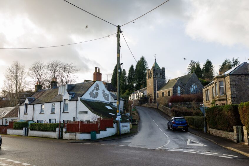 Crossroads in middle of Glenfarg, facing Church Brae, a steep hill with houses on either side and a church halfway up