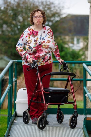 Karen Robertson standing behind her walking frame with wheels outside her home in Invergowrie.