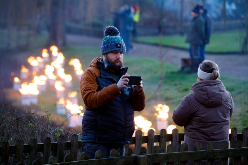 Visitors take selfies as they walk through the fire-lit gardens.