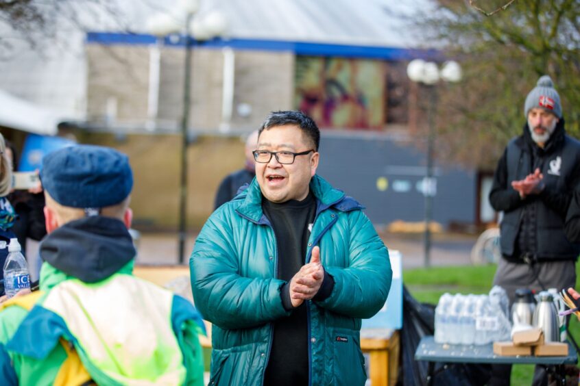 Pete Chan rubbing his hands together and smiling to people standing around outside the North Inch, Perth