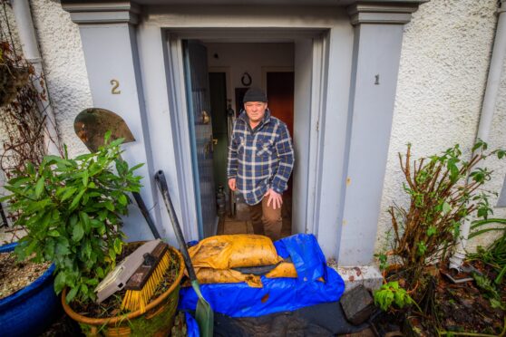 Niall McNab standing at his front door behind mud covered sandbags