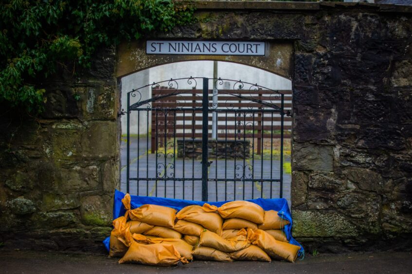 Sandbags piled outside an iron gate with a sign for St Ninian's Court.