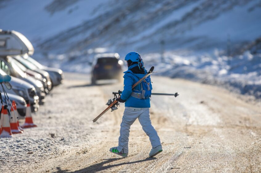 Person in skiwear walking across road to car park at Glenshee ski centre