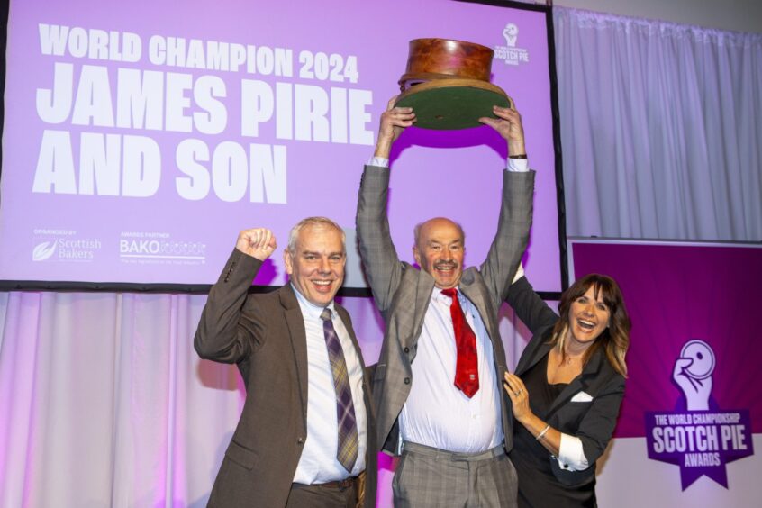 Alan Pirie holding a trophy in the shape of a giant pie on stage with Carol Smillie