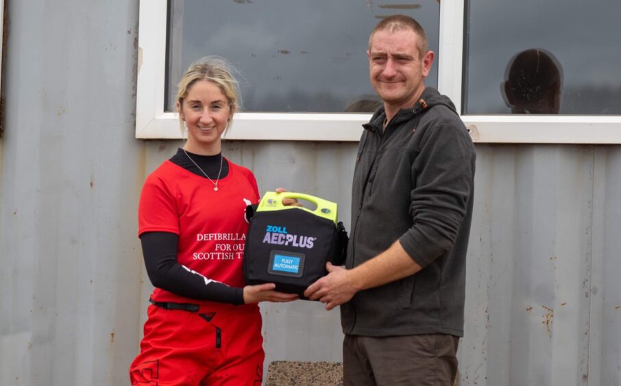 Sara hands over a defibrillator to Craig Hall at Duns Motocross Track.