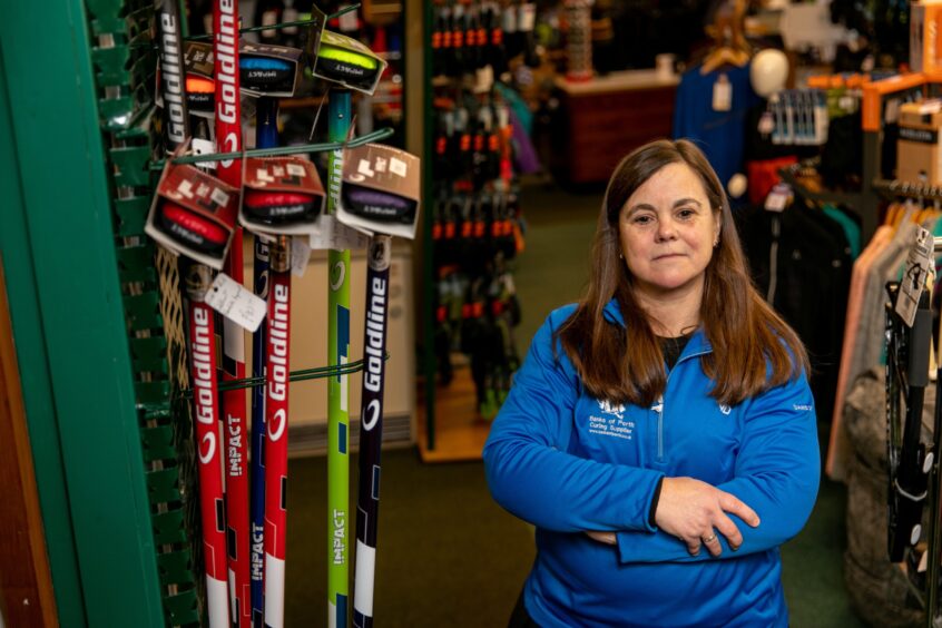 Rona Banks standing next to display of curling brooms and other kit in her Perth shop.