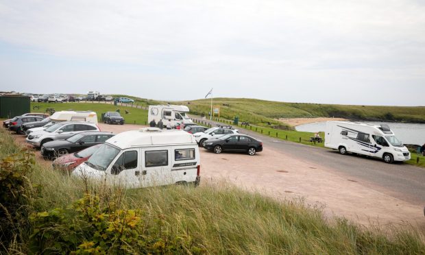 Campervans and cars in a car park beside the sea in Fife