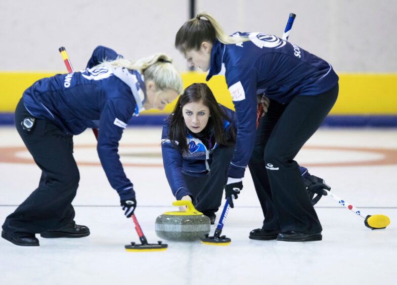 Eve Muirhead and team mates in Scotland team tracksuits curling at the Dewars Centre ice rink in 2017. She s kneeling on the ice looking straight at the camera as she releases the curling stone.