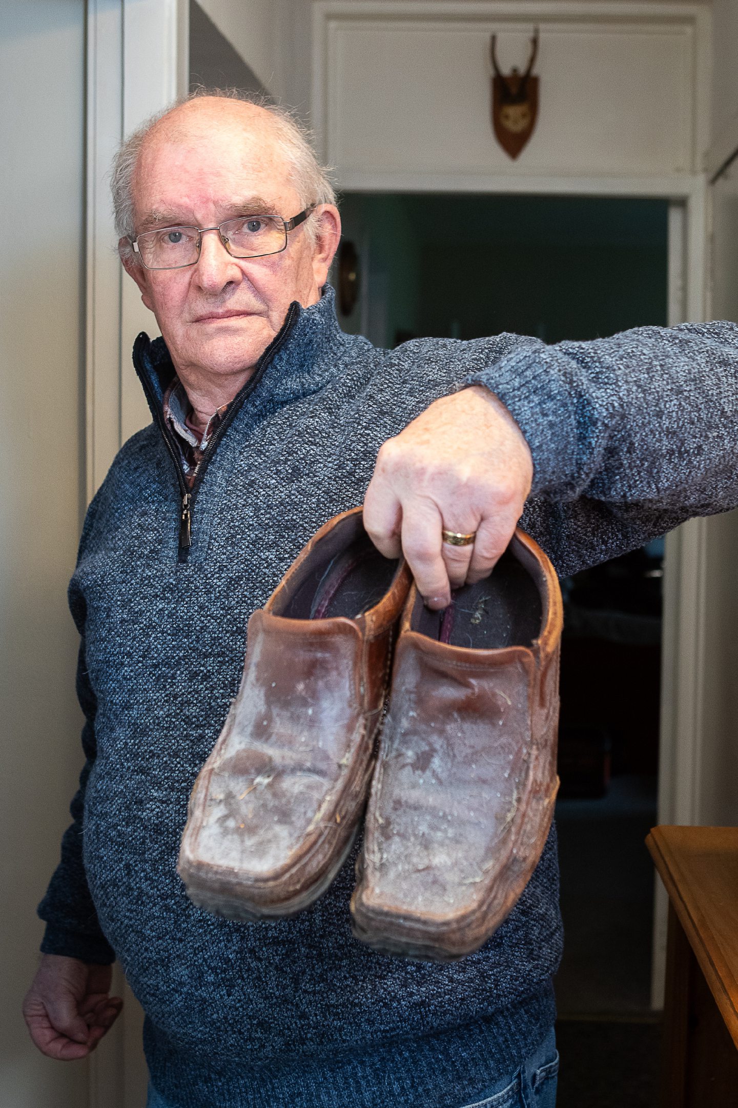 Norman Hawkes, who is complaining about mould in his council house, holding a pair of leather shoes covered in mould.
