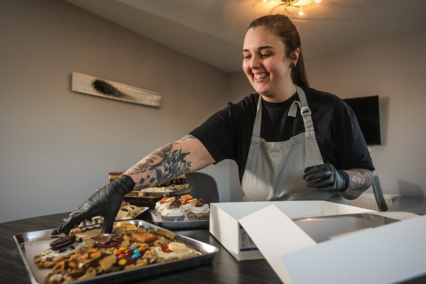 Baked House Co Carnoustie owner packs cookies and other baked goods into a white box for a customer.