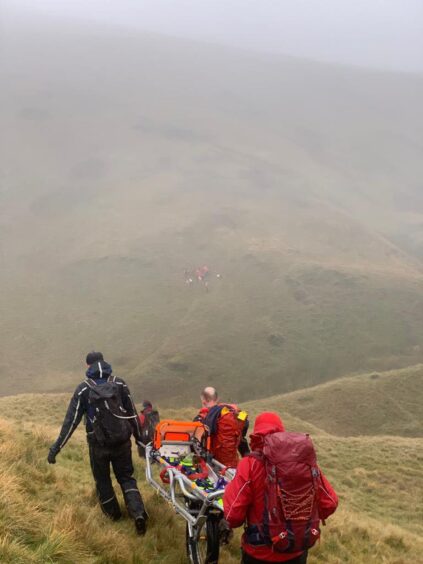 Tayside Mountain Rescue Team members carrying a stretcher across a misty mountainside