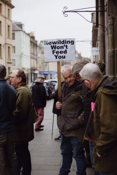 Man holding placard which reads 'rewilding won't feed you'