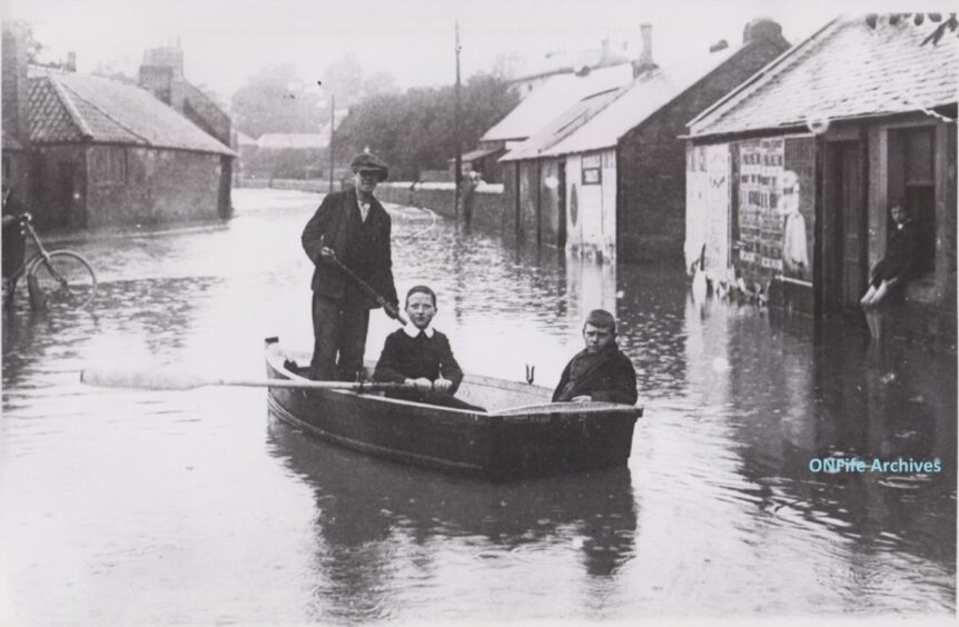 Three boys paddling a boat in Burnside, Cupar, during the floods of July 1916.