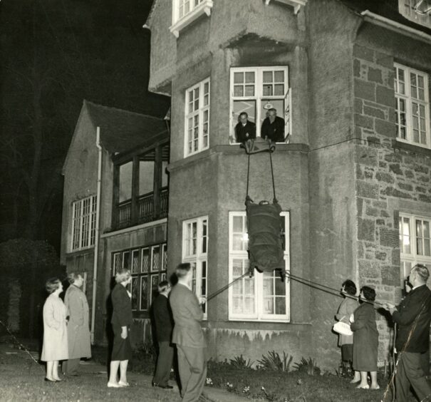 Someone is lowered from a first-floor window as a rescue team goes into action in 1961.