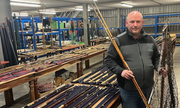 Auctioneer Gordon Delaney standing in front of tables covered in fishing rods