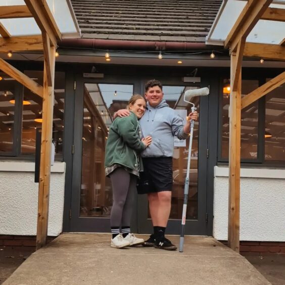 Daisy Walker and Liam Turnbull, holding a paint roller and hugging on the doorstep of their new cafe premises in Pitlochry
