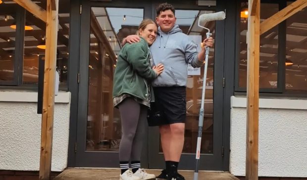 Daisy Walker and Liam Turnbull standing at door to Jessie's Cafe. Daisy has her arms around Liam and he is holding a paint roller.