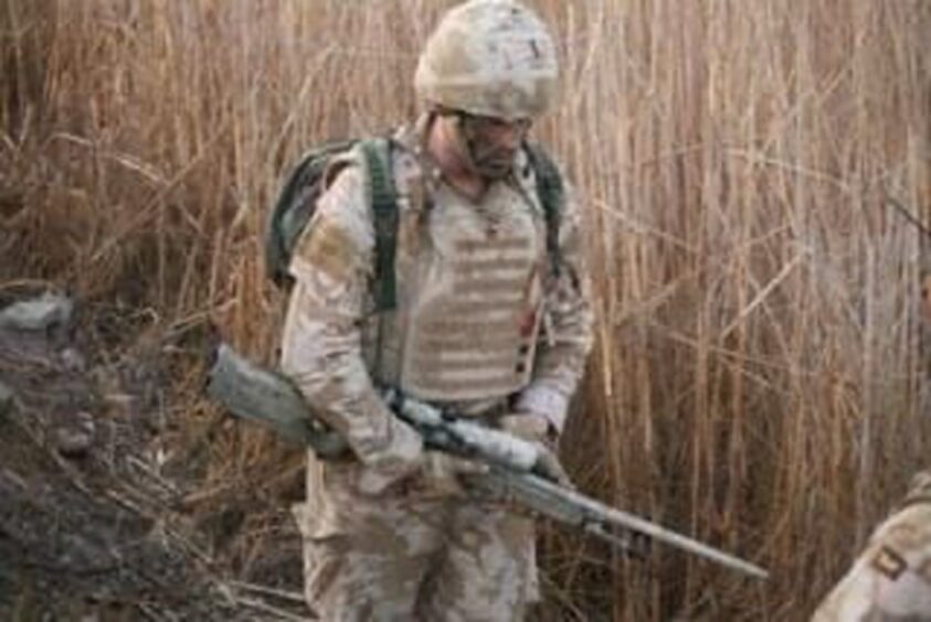 Mark Harding during his army days, carrying a gun and walking through a field