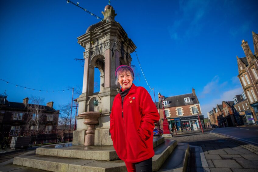 June McEwan smiling next to Murray Fountain in James Square, Crieff.