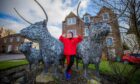 June McEwan giving two thumbs up next to metal Highland sculptures depicting a Highland cow, bull and calf in Crieff.