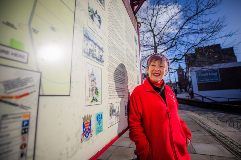 June McEwan smiling next to tourist map in James Square, Crieff.