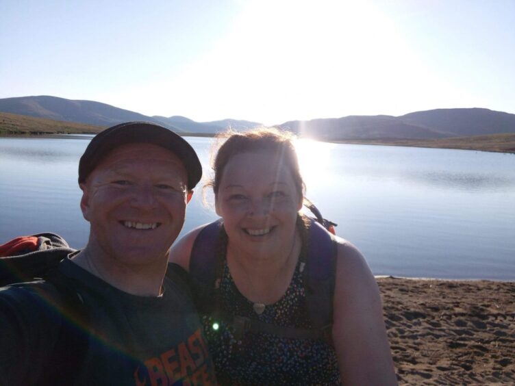Dundee couple Karen and Andy McDermott, smiling before a lake, are taking on the Cateran Yomp with their daughters and partners.