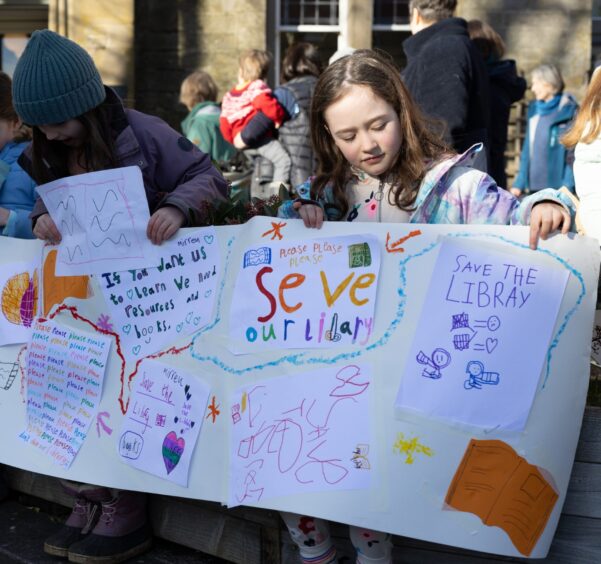 Young girl holding hand-drawn 'save our library' banner