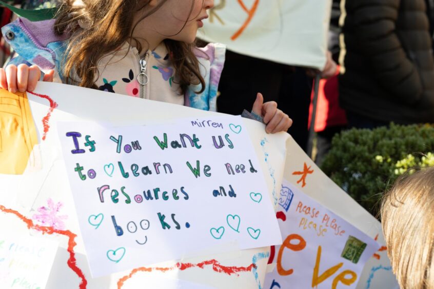 Young girl holding hand drawn banner which reads 'if you want us to learn we need resources and books'