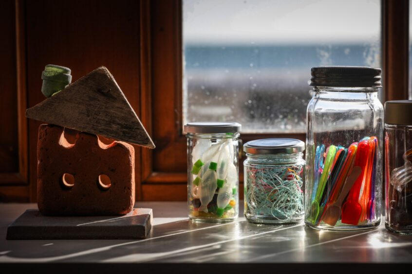 Image shows Cat Coulter's studio in Cellardyke. Jars filled with plastic objects found on the beach sit on a sunny windowsill.