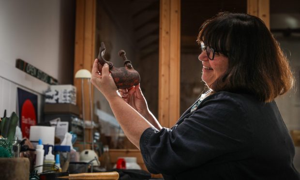 Image shows artist Cat Coulter in her Cellardyke studio. Cat is sitting at her desk working on a new crab created from found objects.