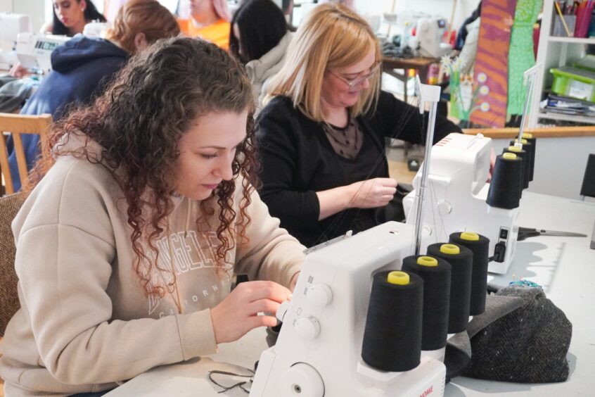 Image shows: Amy Deans working at a sewing machine. Amy learned how to sew as part of the Dundee charity Front Lounge's Kindred Clothing project.