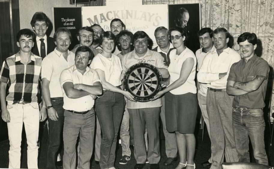 Darts great Jocky Wilson holds a dartboard surrounded by those who took part in a charity darts evening at the Angus.