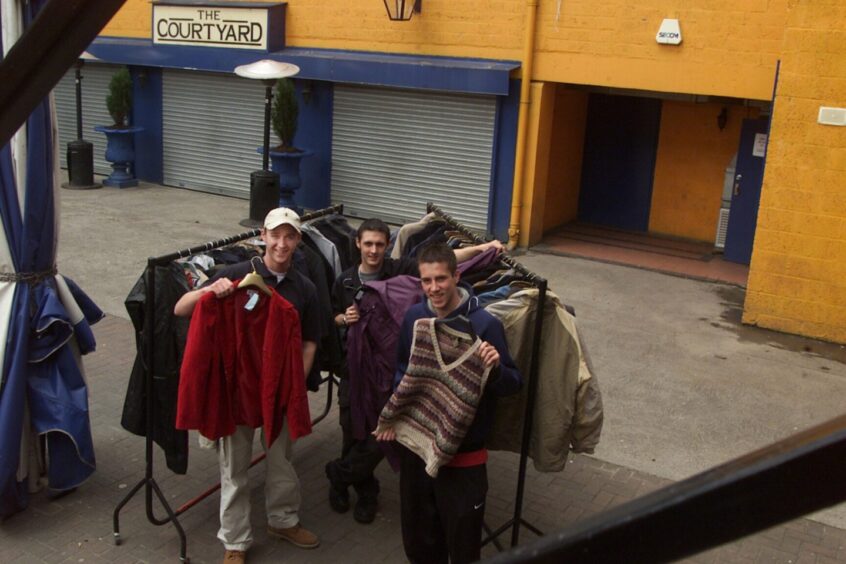 Three Ice Factory staff beside two rails of clothing show off the unclaimed jackets and clothing left behind in 2002.